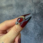 Hand wearing a silver ring with a red garnet stone against a gray background